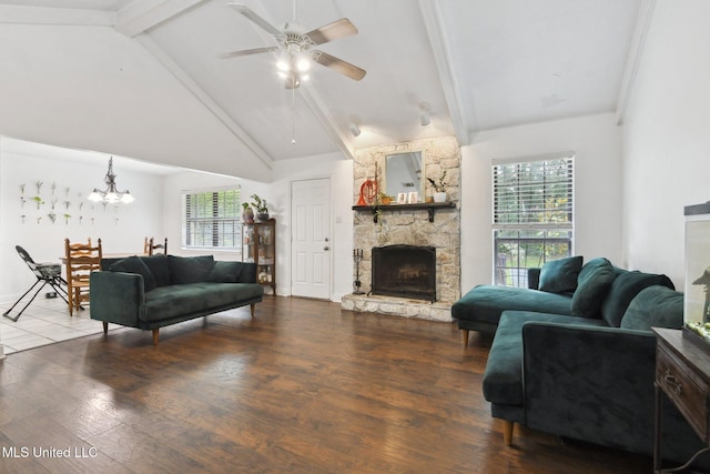 living room with vaulted ceiling with beams, ceiling fan with notable chandelier, a stone fireplace, and wood finished floors