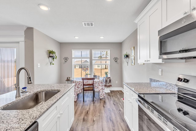 kitchen with sink, appliances with stainless steel finishes, white cabinetry, light stone countertops, and light wood-type flooring