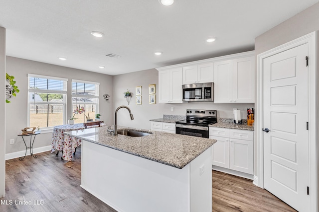 kitchen featuring sink, white cabinetry, light stone counters, a center island with sink, and stainless steel appliances