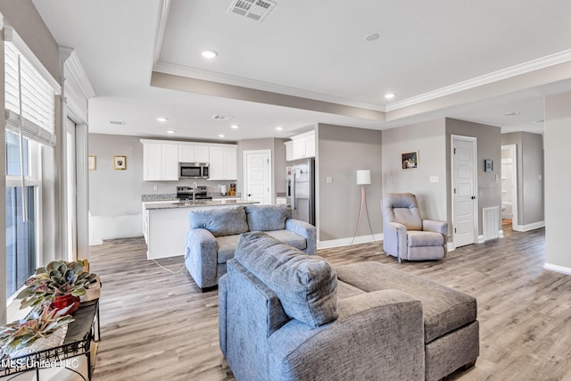 living room with ornamental molding, light hardwood / wood-style floors, and a tray ceiling