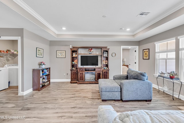 living room featuring ornamental molding, a tray ceiling, separate washer and dryer, and light wood-type flooring