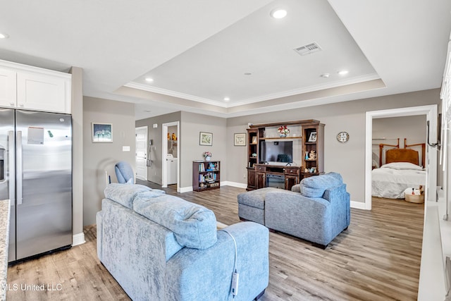 living room featuring ornamental molding, a raised ceiling, and light wood-type flooring