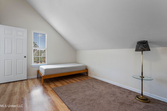 bedroom with a textured ceiling, vaulted ceiling, and hardwood / wood-style flooring