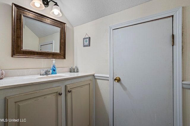 bathroom featuring vanity, vaulted ceiling, and a textured ceiling