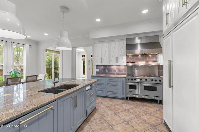 kitchen with sink, tasteful backsplash, double oven range, white cabinets, and wall chimney range hood