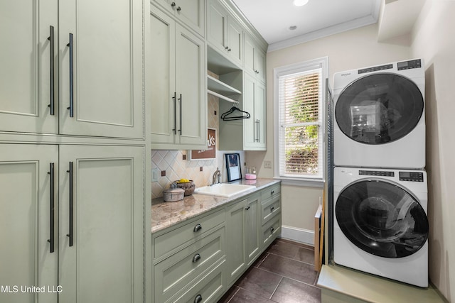 laundry room featuring cabinets, sink, stacked washer / dryer, ornamental molding, and dark tile patterned floors