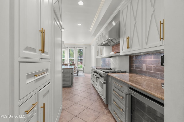 kitchen with double oven range, wall chimney exhaust hood, light tile patterned floors, light stone countertops, and wine cooler