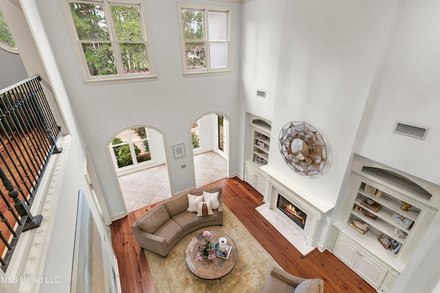 living room featuring a high ceiling, built in features, wood-type flooring, and a healthy amount of sunlight