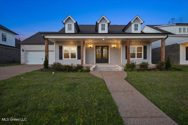 view of front of house featuring a garage, a yard, covered porch, and french doors