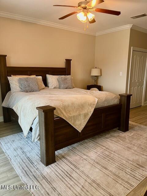 bedroom with ornamental molding, visible vents, light wood-style flooring, and a ceiling fan