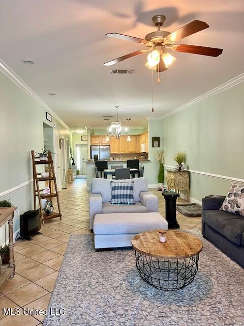 living area with light tile patterned floors, ceiling fan with notable chandelier, visible vents, baseboards, and ornamental molding