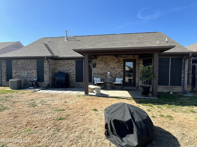 back of house with brick siding, roof with shingles, a patio area, and cooling unit