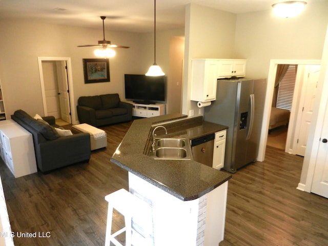 kitchen featuring a peninsula, a sink, white cabinetry, appliances with stainless steel finishes, and dark countertops