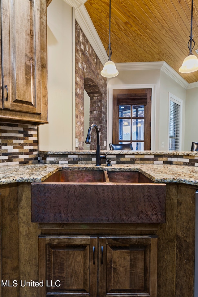 kitchen with sink, light stone counters, ornamental molding, and decorative light fixtures