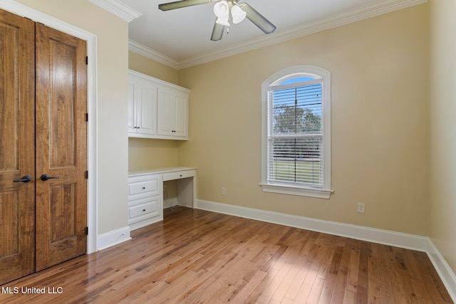 unfurnished office featuring built in desk, light hardwood / wood-style floors, ornamental molding, and ceiling fan