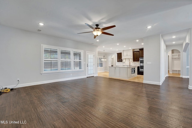 unfurnished living room featuring sink, ceiling fan with notable chandelier, and dark hardwood / wood-style floors