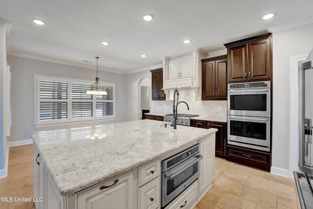 kitchen featuring ornamental molding, backsplash, double oven, and a center island with sink