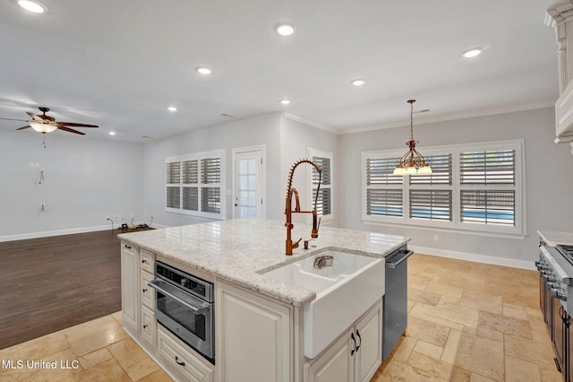 kitchen with light stone countertops, pendant lighting, stainless steel appliances, sink, and a center island with sink