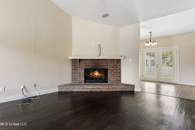 unfurnished living room with french doors, an inviting chandelier, a fireplace, and hardwood / wood-style floors