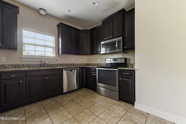 kitchen with sink, appliances with stainless steel finishes, light tile patterned flooring, and dark stone counters