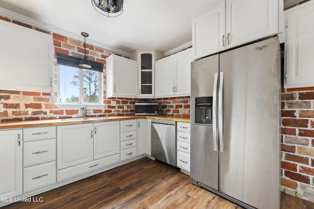 kitchen featuring pendant lighting, brick wall, white cabinets, appliances with stainless steel finishes, and sink