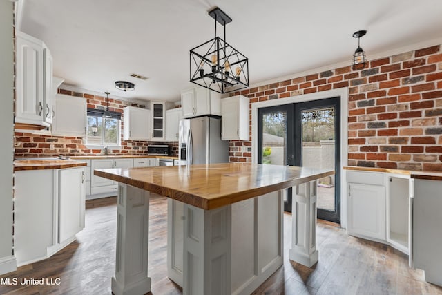 kitchen with wooden counters, hanging light fixtures, a center island, stainless steel fridge, and white cabinets