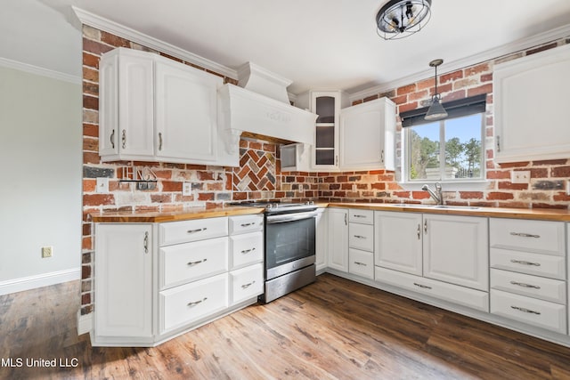 kitchen featuring stainless steel stove, pendant lighting, butcher block counters, white cabinets, and sink