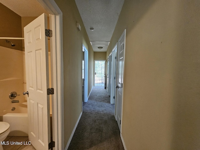 hall featuring dark colored carpet and a textured ceiling