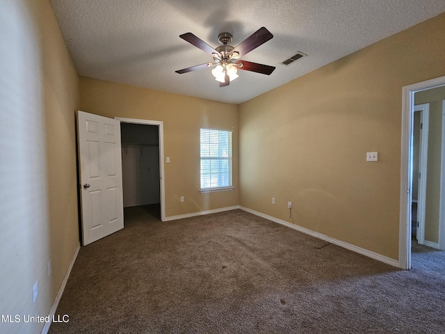 unfurnished bedroom featuring ceiling fan, a spacious closet, carpet floors, a textured ceiling, and a closet