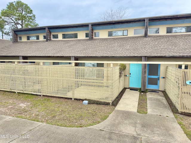 view of front of property featuring roof with shingles, fence, and stucco siding