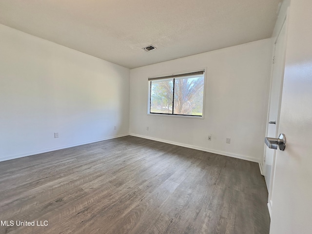 unfurnished room featuring dark wood-type flooring, visible vents, a textured ceiling, and baseboards