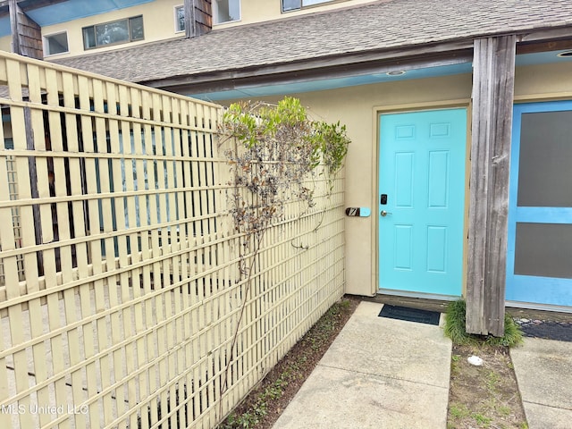 entrance to property with roof with shingles and stucco siding