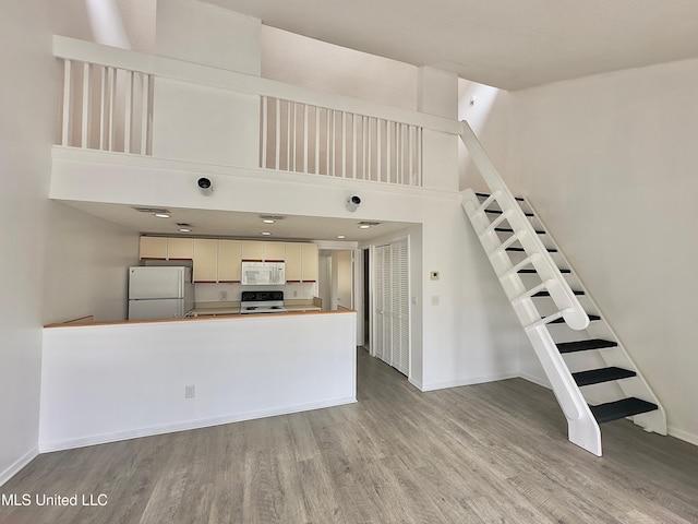 kitchen with white appliances, wood finished floors, a towering ceiling, and baseboards