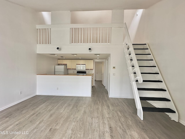 unfurnished living room featuring baseboards, light wood-style flooring, and a high ceiling