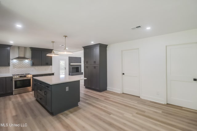 kitchen with stainless steel electric stove, decorative backsplash, light countertops, wall chimney range hood, and light wood-type flooring