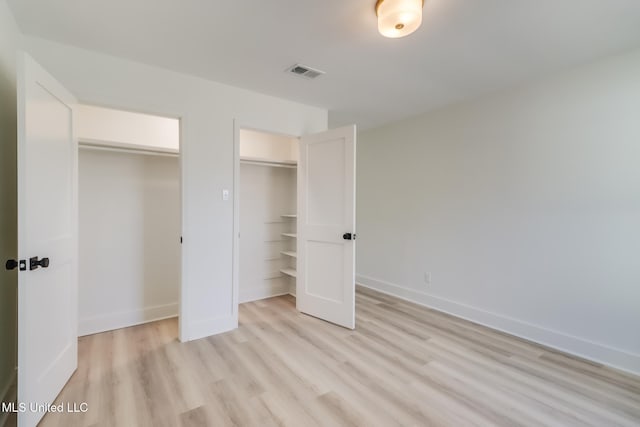 unfurnished bedroom with visible vents, baseboards, light wood-style floors, and multiple closets