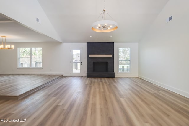 unfurnished living room featuring a healthy amount of sunlight, a chandelier, a fireplace, and light wood finished floors