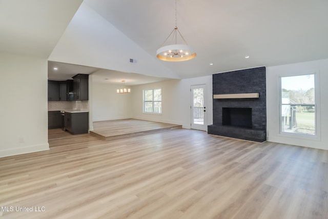 unfurnished living room with baseboards, visible vents, light wood-style flooring, a brick fireplace, and a chandelier