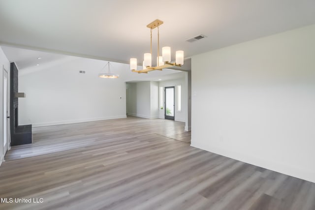 empty room with a chandelier, visible vents, light wood-style flooring, and a large fireplace