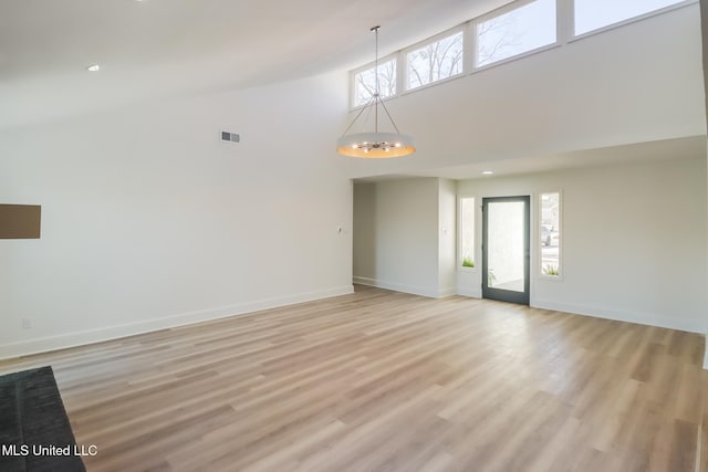 unfurnished living room with baseboards, an inviting chandelier, and light wood-style flooring