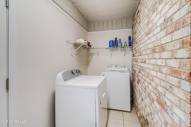 laundry area with light tile patterned floors, brick wall, and washing machine and clothes dryer