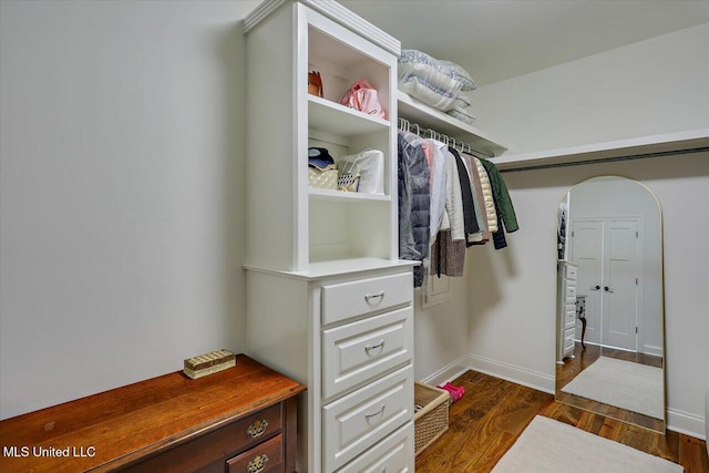 walk in closet with arched walkways and dark wood-style flooring