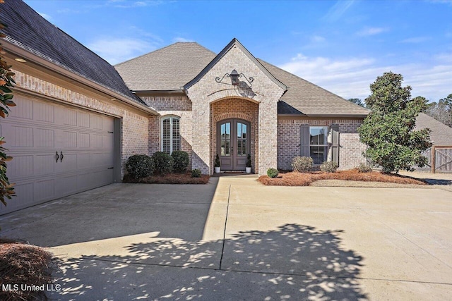 french provincial home featuring concrete driveway, french doors, brick siding, and roof with shingles