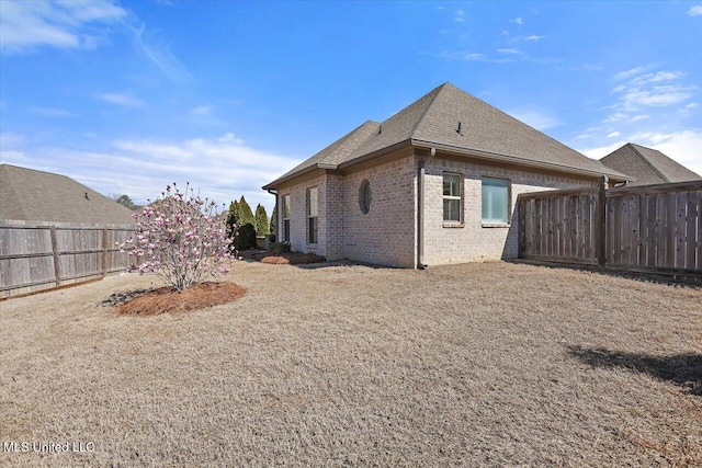 back of property featuring brick siding, roof with shingles, and a fenced backyard