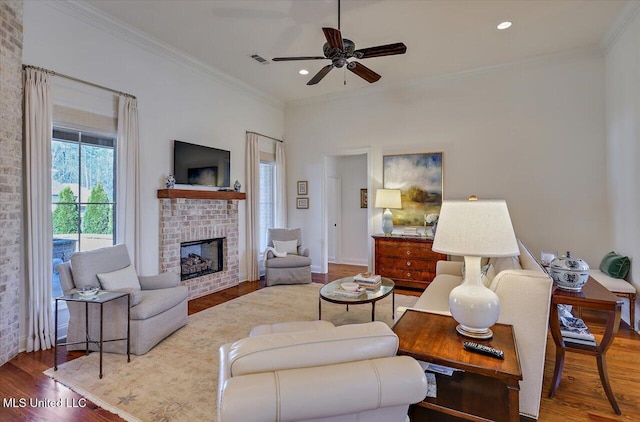 living room featuring visible vents, a brick fireplace, crown molding, and wood finished floors