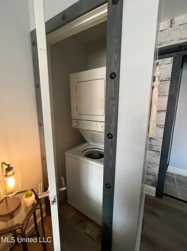 clothes washing area featuring hardwood / wood-style floors, stacked washer and dryer, and a barn door