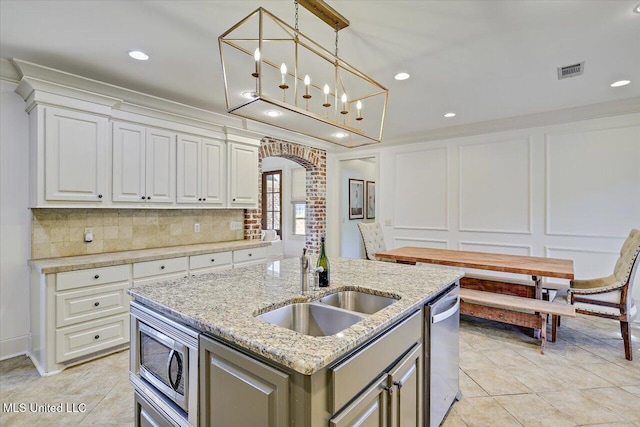 kitchen featuring appliances with stainless steel finishes, a sink, a kitchen island with sink, arched walkways, and visible vents