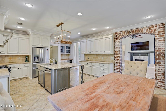 kitchen with crown molding, ceiling fan, appliances with stainless steel finishes, and a kitchen island with sink