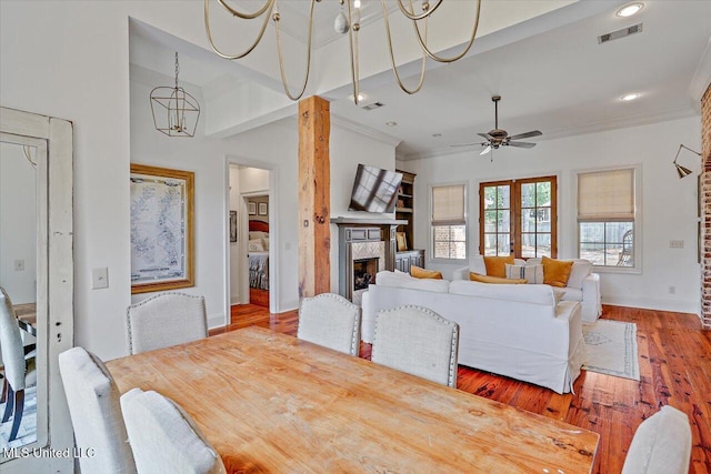 dining area featuring crown molding, a fireplace, ceiling fan with notable chandelier, baseboards, and visible vents