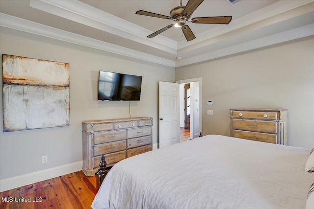 bedroom with baseboards, ceiling fan, wood finished floors, and a tray ceiling
